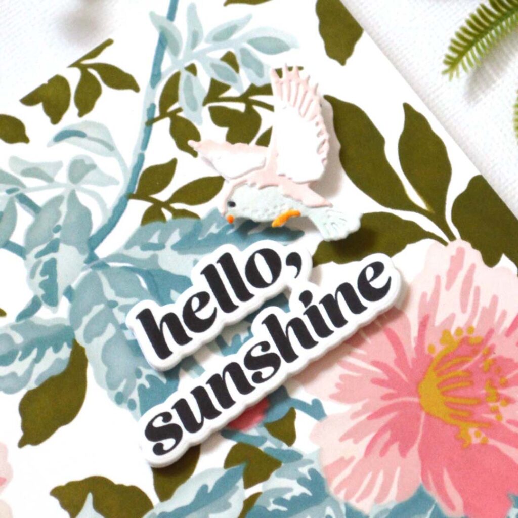 Layered bird die card coloured with alcohol markers on a soft ink blended leafy background with a central popped up stamped sentiment by Therese Calvird