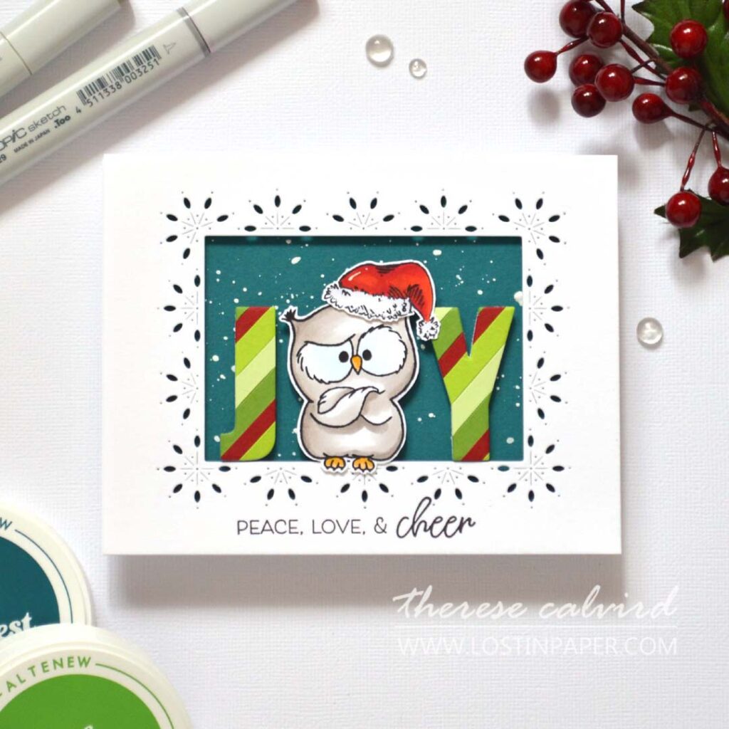 Humorous owl with Santa hat used as the “O” in JOY; letters die-cut from striped paper, owl in a decorative frame window over a teal snowy background.