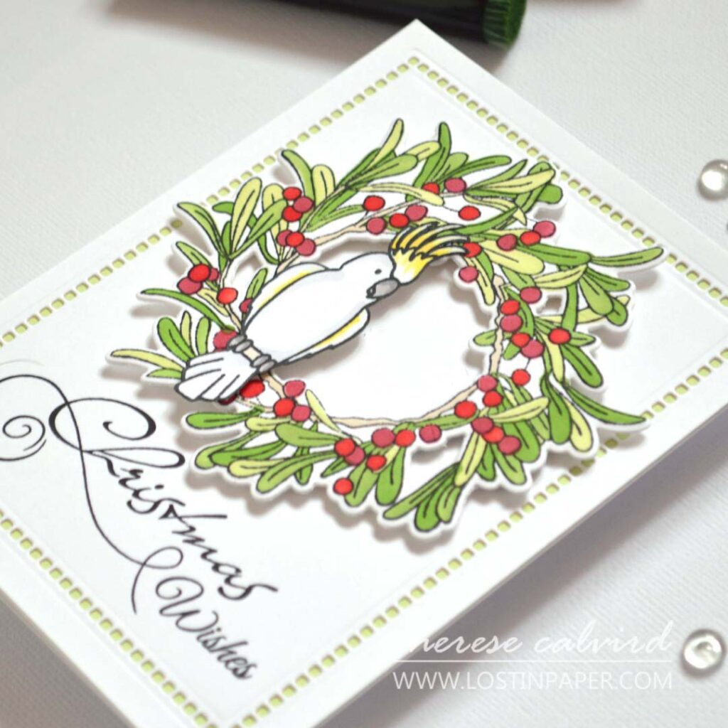 Stamped and alcohol-marker colored bird on a stamped and ink-blended wreath, stepped up with a cockatoo and a die-cut negative space border