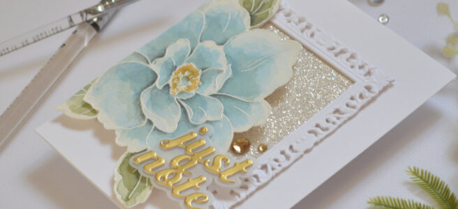 Handmade card featuring an ornate picture frame with glitter paper and a large blue watercolor bloom by Therese Calvird