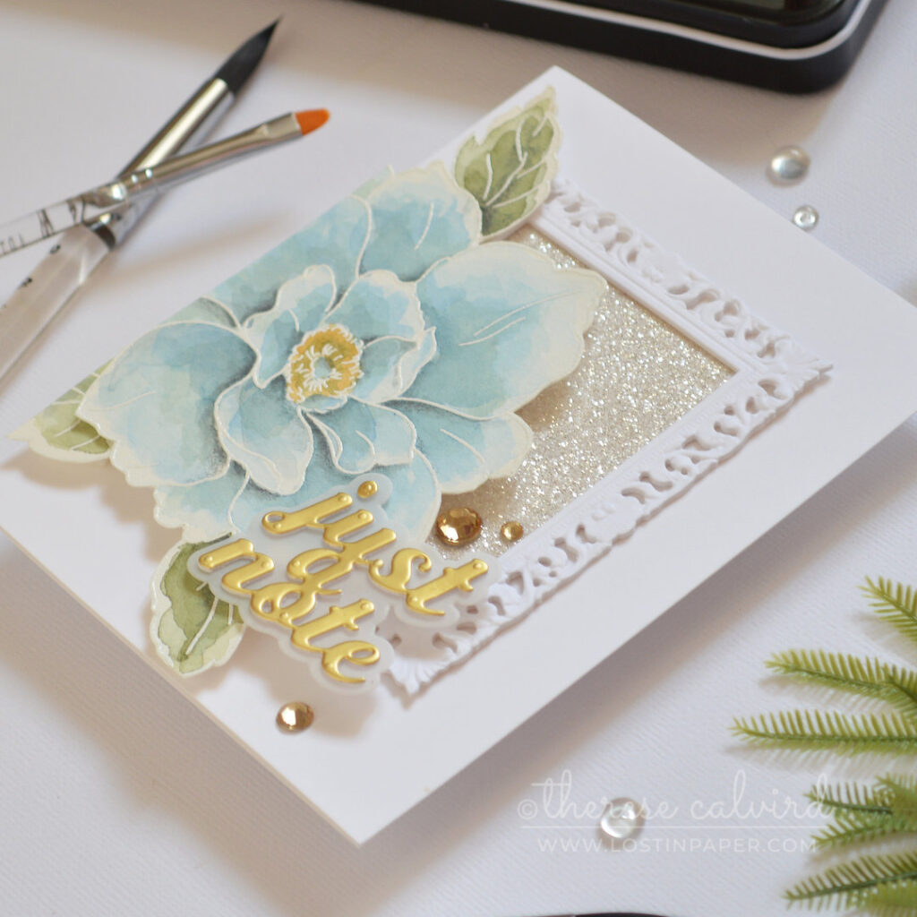 Handmade card featuring an ornate picture frame with glitter paper and a large blue watercolor bloom by Therese Calvird