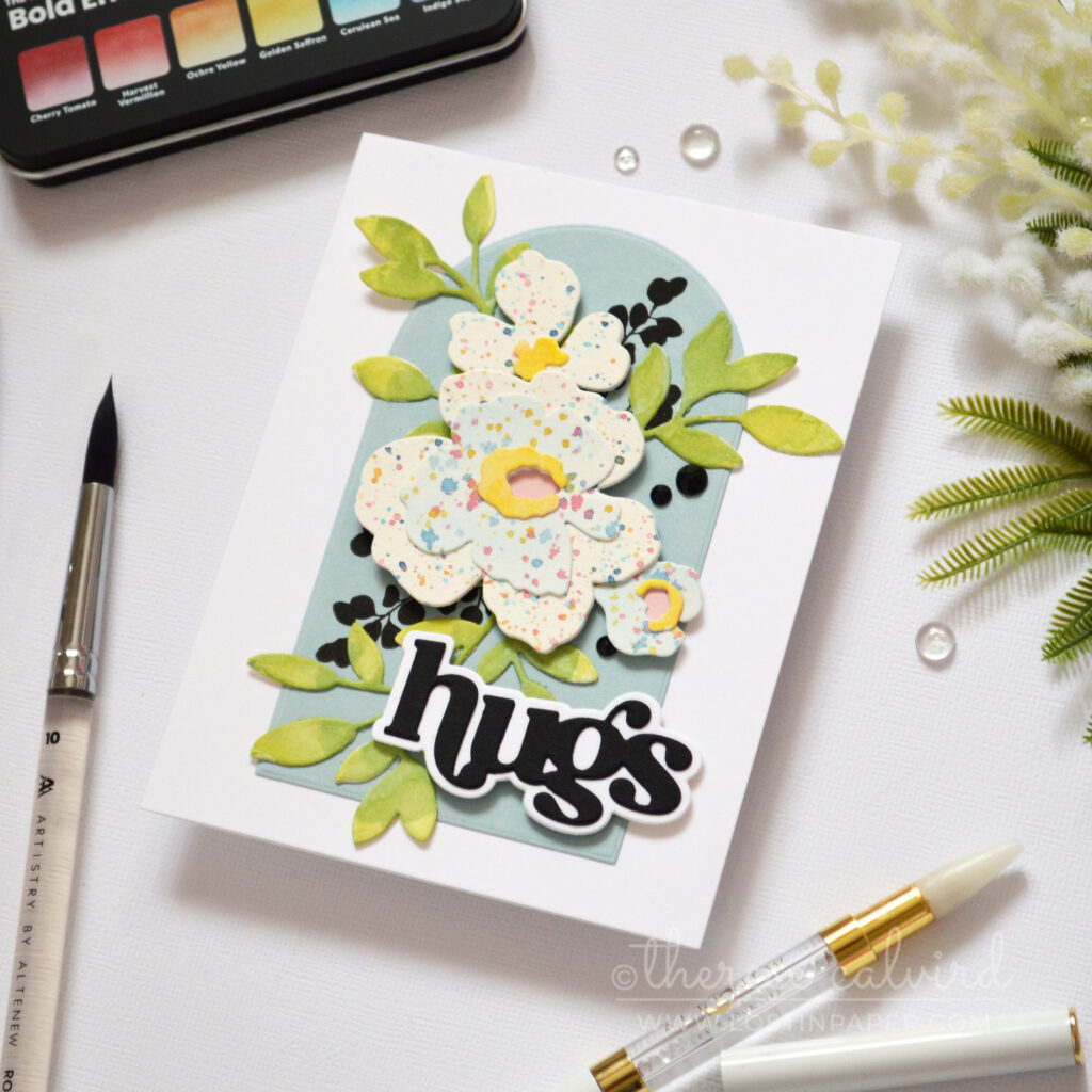 Watercolor splattered floral shapes arranged as a bouquet on an arched panel with a bold die cut sentiment