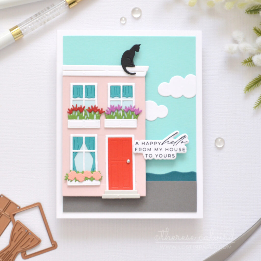 A2 handmade card featuring a trimmed Everyday City Holiday die cut pink house with flower boxes, rooftop cat, seaside scene and clouds by Therese Calvird