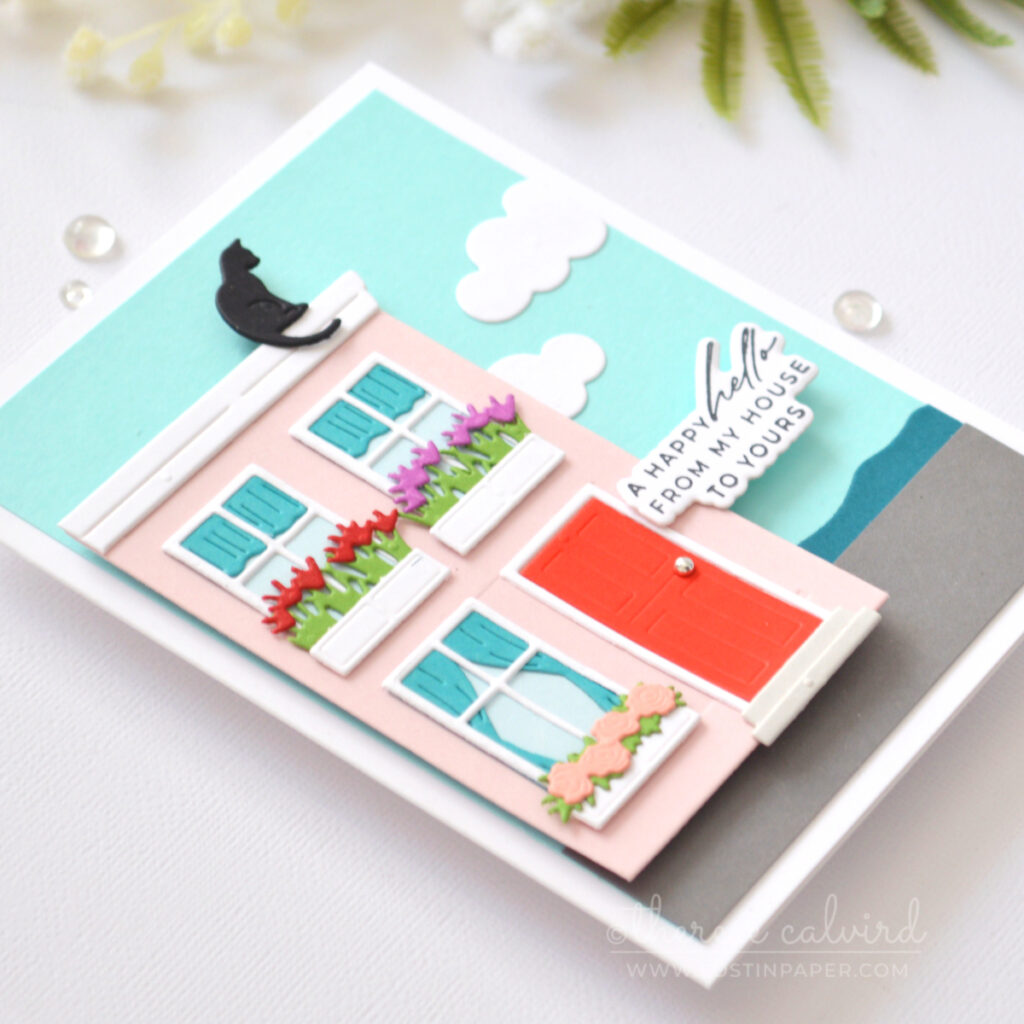 A2 handmade card featuring a trimmed Everyday City Holiday die cut pink house with flower boxes, rooftop cat, seaside scene and clouds by Therese Calvird