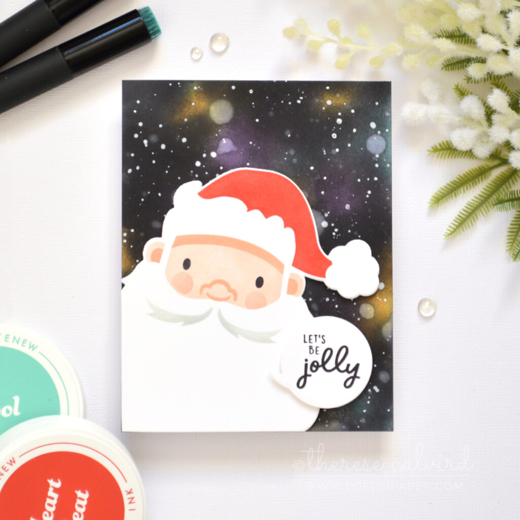 Christmas card with an ink-blended galaxy background, white splattered stars, and a large stenciled Santa face with a Jolly sentiment.