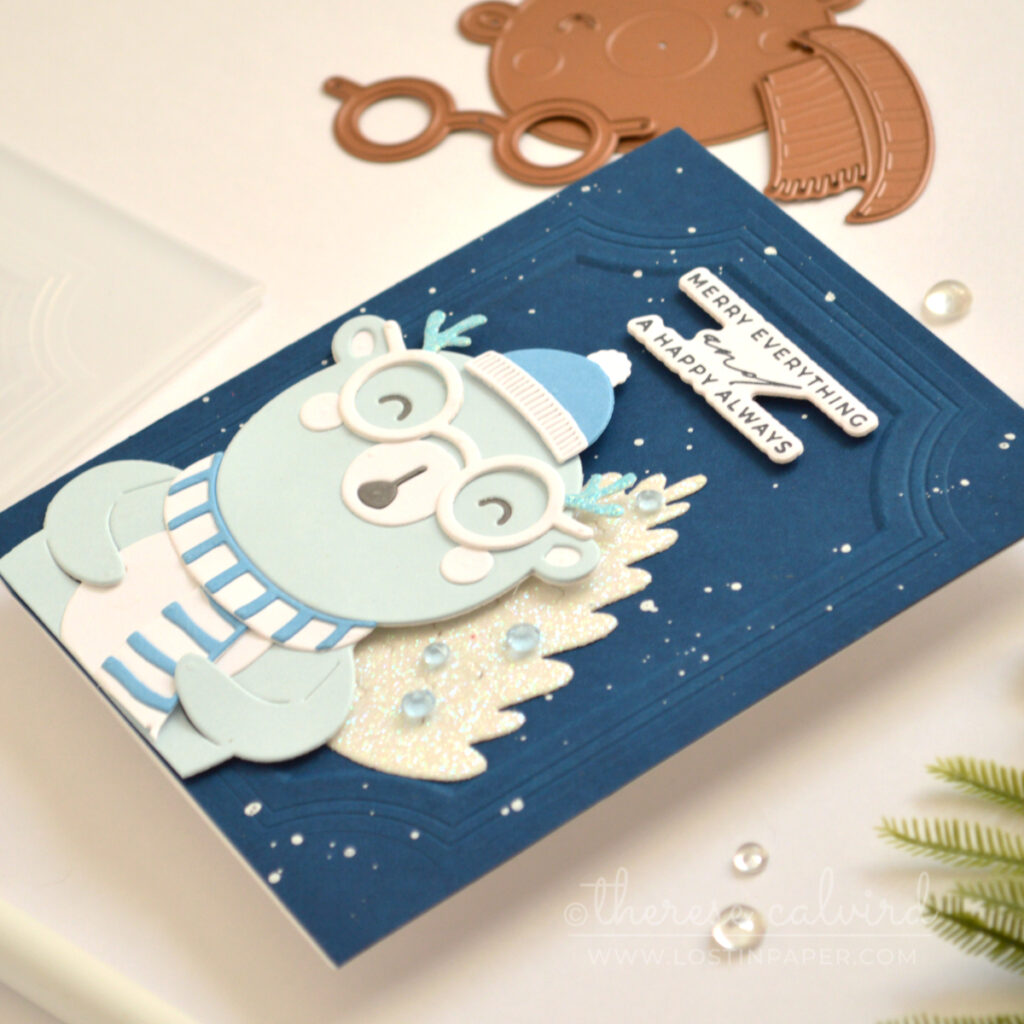Blue bear Christmas card with a glittery white tree and dark blue embossed background.