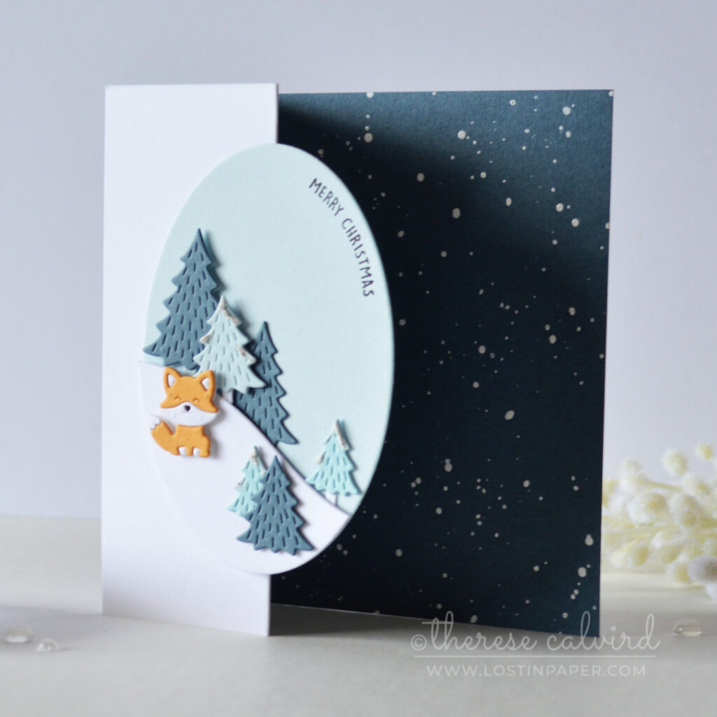Blue Z-fold Christmas card with snowy trees, oval scene and orange fox by Therese Calvird