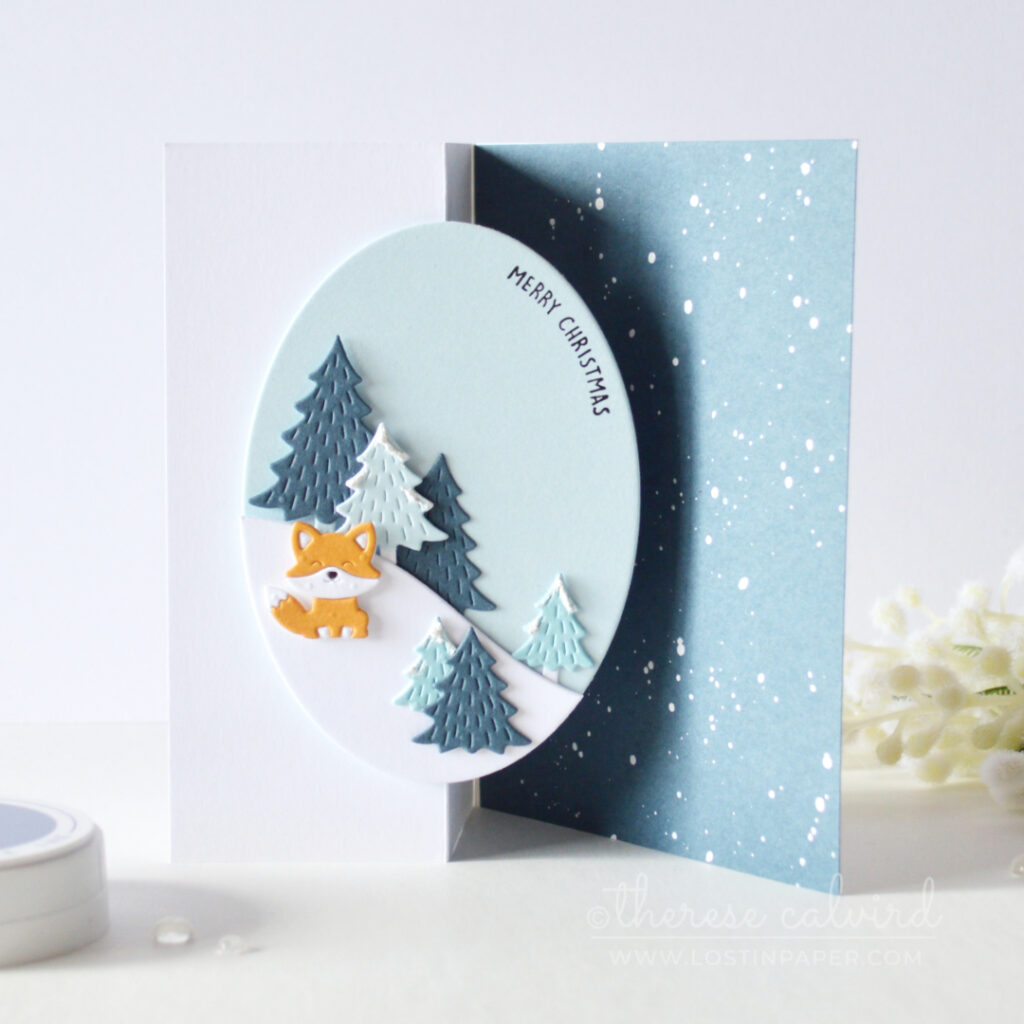 Blue Z-fold Christmas card with snowy trees, oval scene and orange fox by Therese Calvird