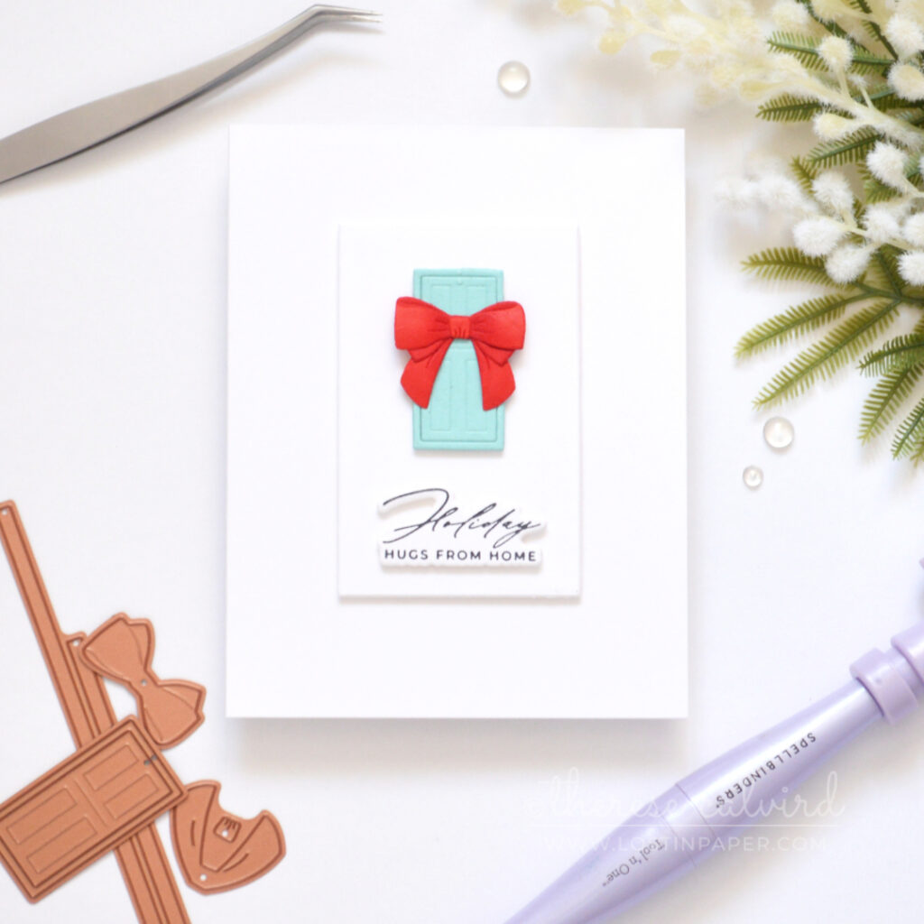 Clean and simple Christmas card with a blue door, dimensional red bow and sentiment on a white background.