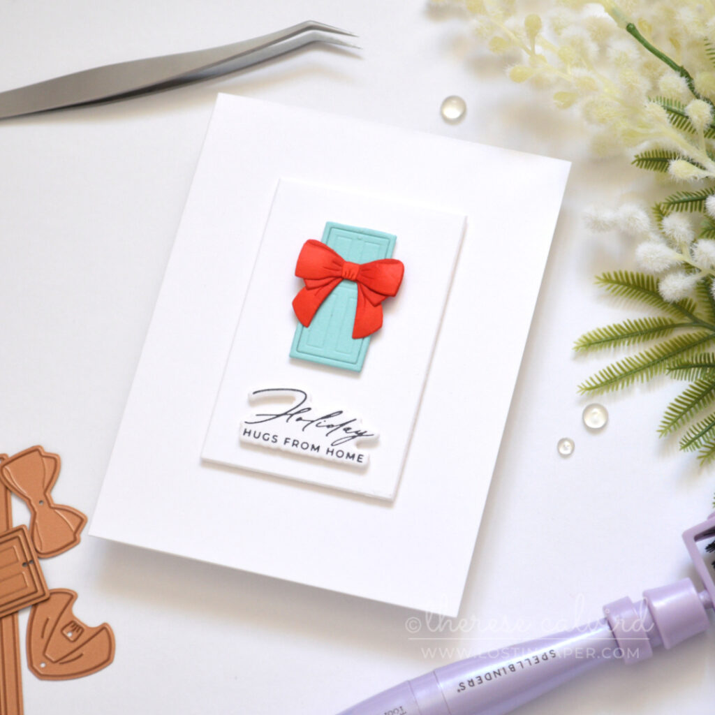 Clean and simple Christmas card with a blue door, dimensional red bow and sentiment on a white background.