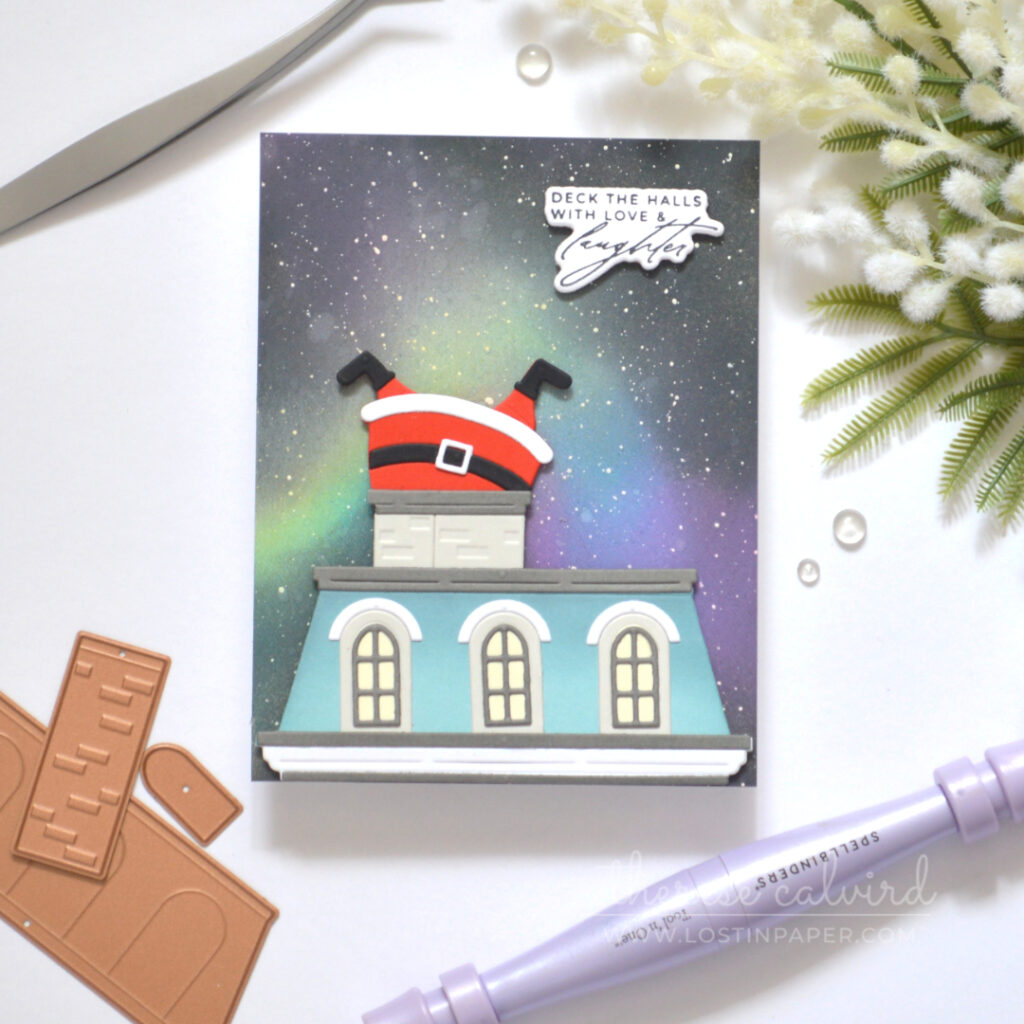 Christmas card with a blue Mansard roof, Northern Lights background and Santa stuck headfirst in a wide chimney.
