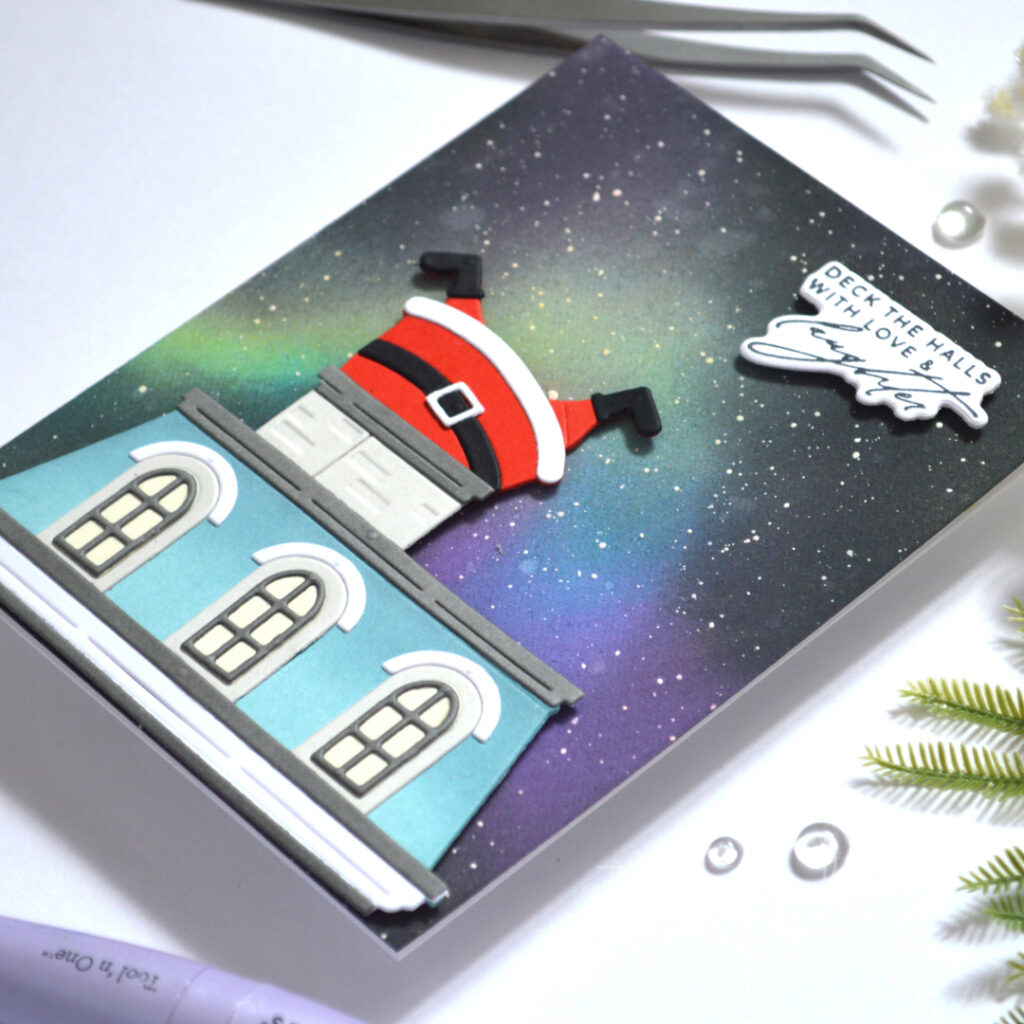 Christmas card with a blue Mansard roof, Northern Lights background and Santa stuck headfirst in a wide chimney.