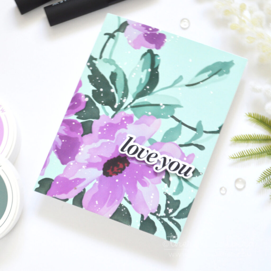 Handmade card with a large purple stenciled flower and teal foliage on pale teal cardstock, with a bold sentiment and white ink splatters.