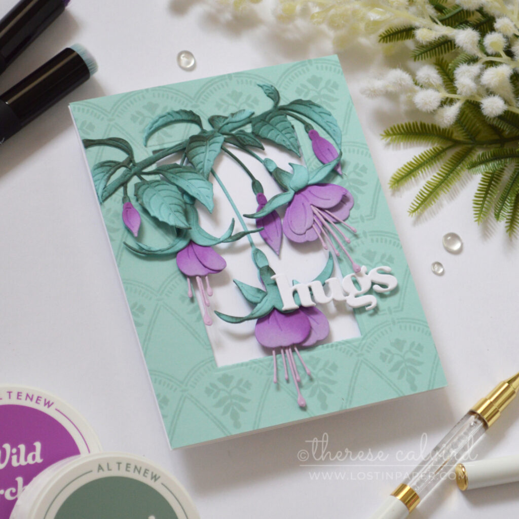 Handmade card with purple fuchsia flowers and teal leaves on a pale teal tone-on-tone stamped frame, finished with a white die-cut “hugs” sentiment.