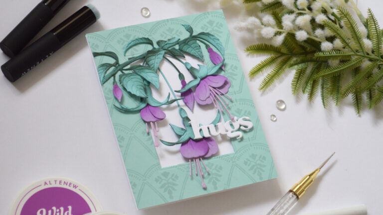 Handmade card with purple fuchsia flowers and teal leaves on a pale teal tone-on-tone stamped frame, finished with a white die-cut “hugs” sentiment.