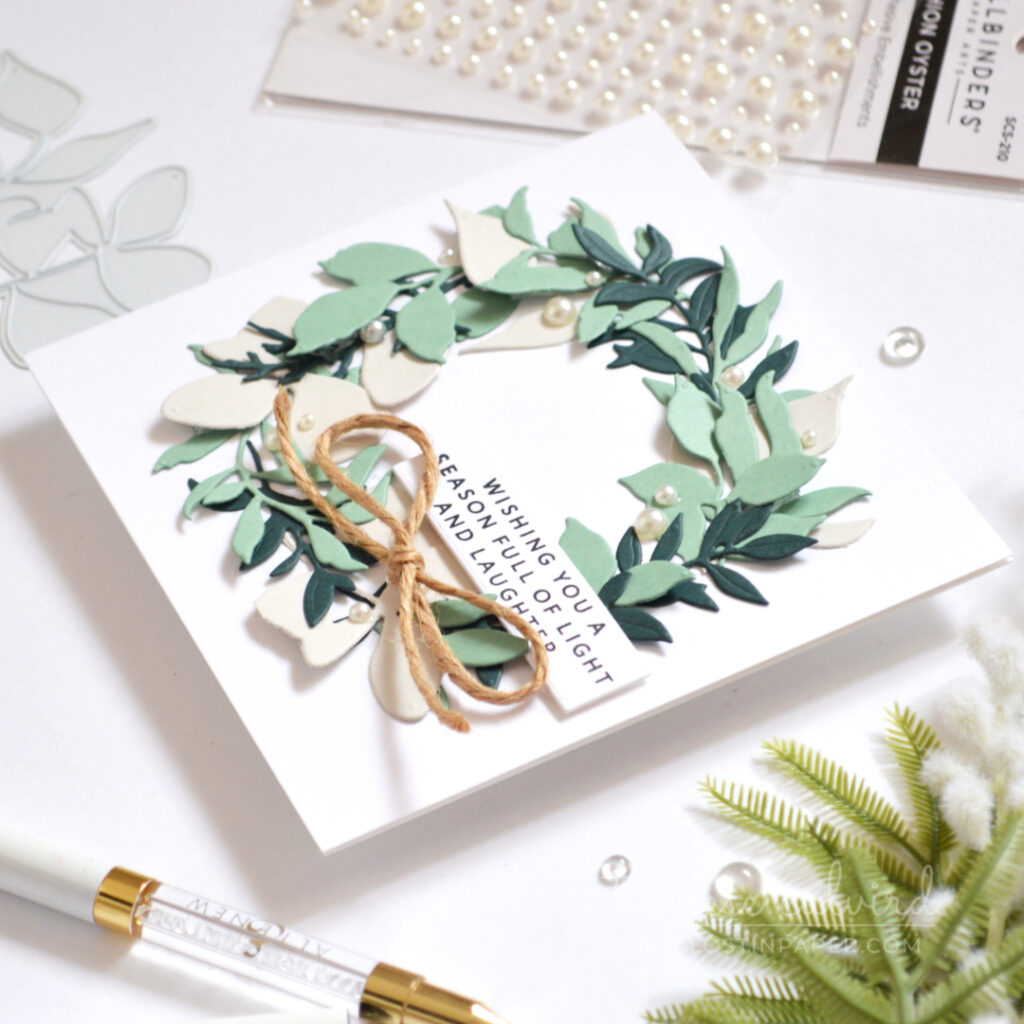 Christmas wreath card with layered eucalyptus-coloured leaves, pearls and twine bow.