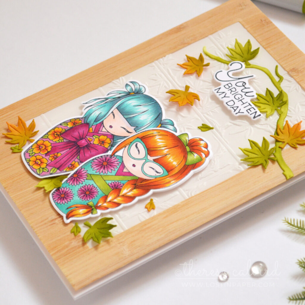 Two colourful Kokeshi girls framed by woodgrain and embossed vellum.