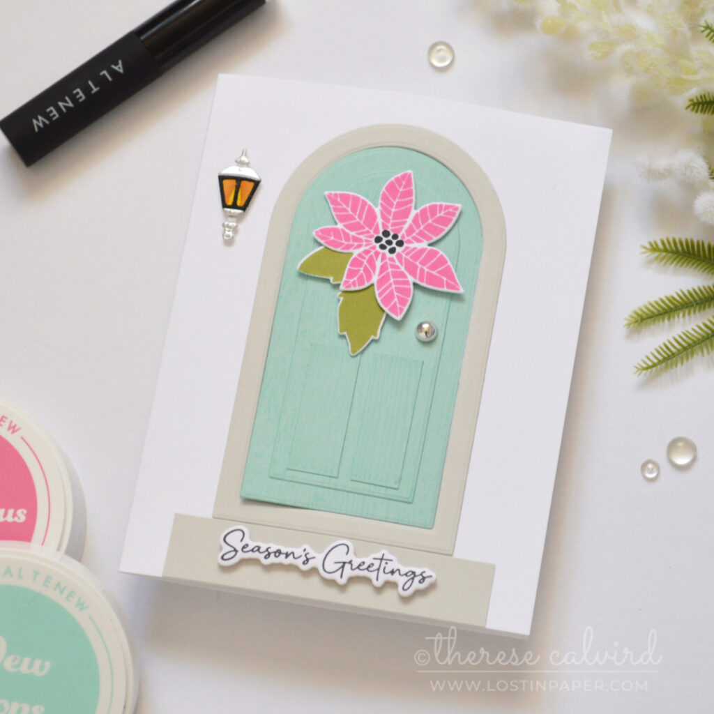 Interactive fun fold Christmas card with a light teal door, pink poinsettia, green leaves, lantern and silver door knob.